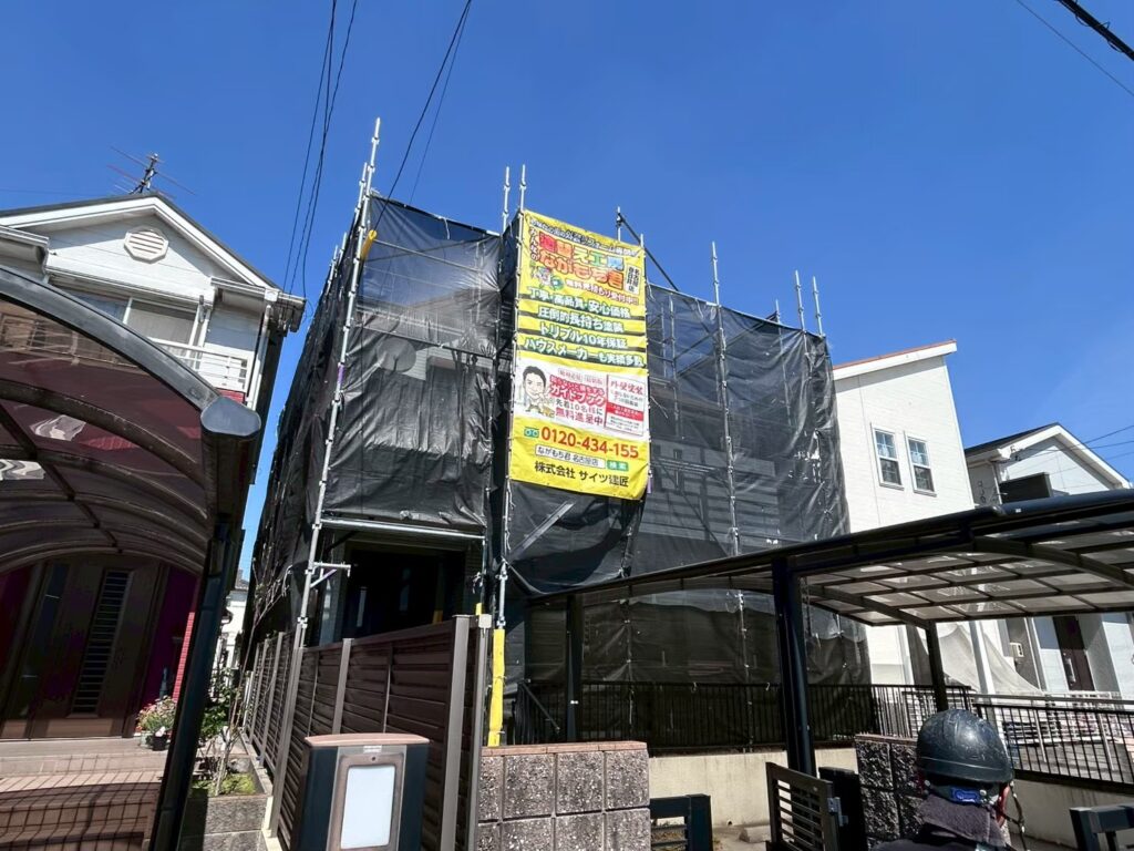 【足場設置・メッシュシート展開】<br />
職人が安全かつ精密な作業を行うための足場を組み立てました。近隣の皆様へ塗料や水が飛散するのを防ぐため、お家全体をしっかりとメッシュシートで囲い、配慮を徹底します。